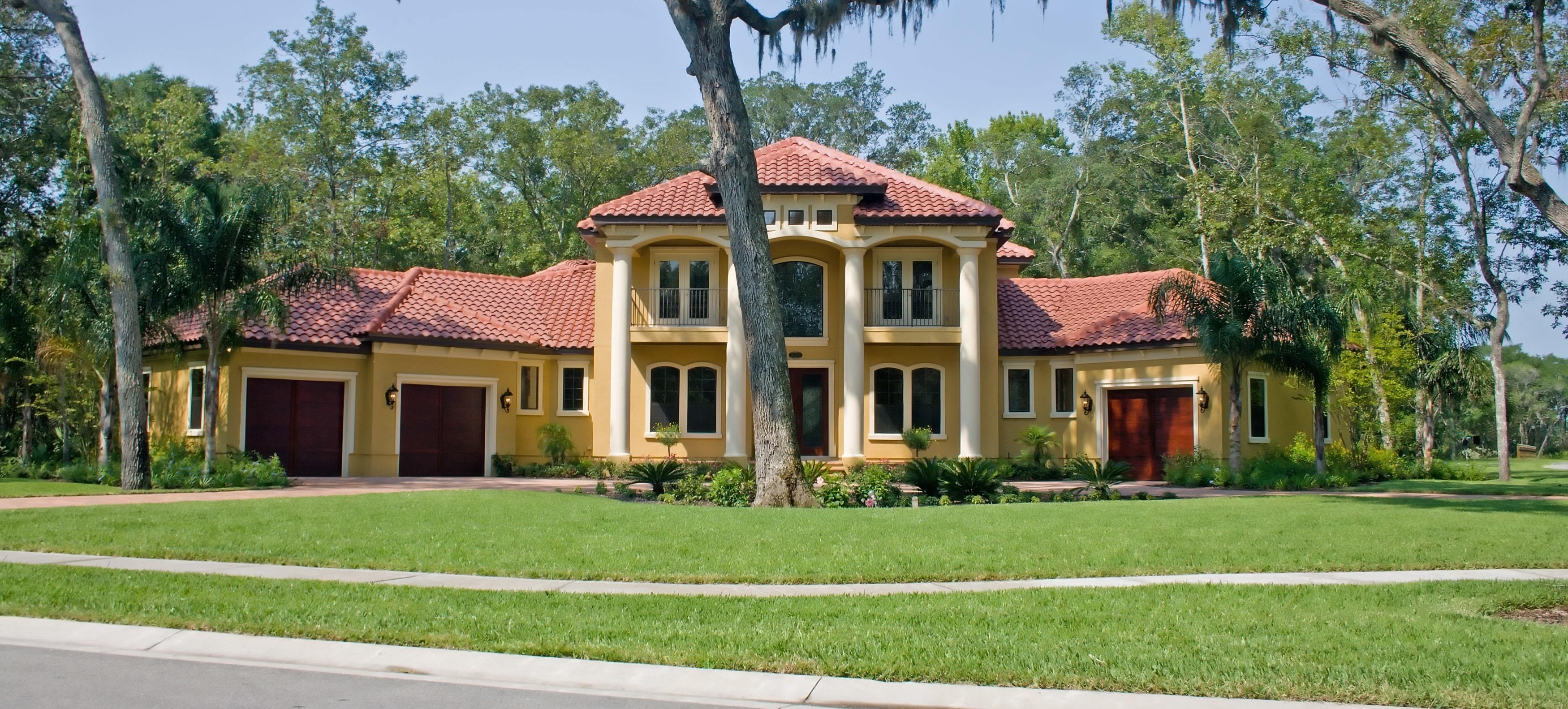 Tile roofed luxury estate style home under shady oak trees in Riverstone, FL.
